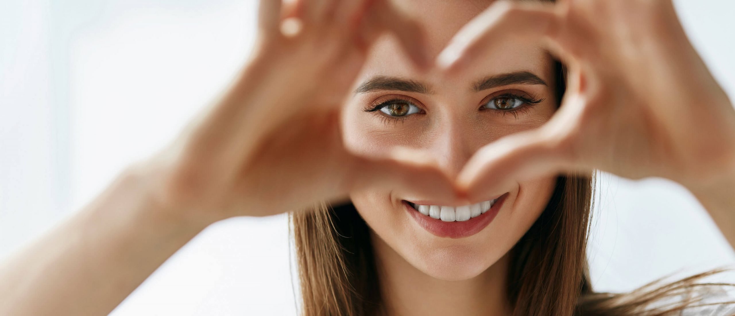 Jeune femme qui sourit en formant un coeur avec ses doigts, chirurgie au laser