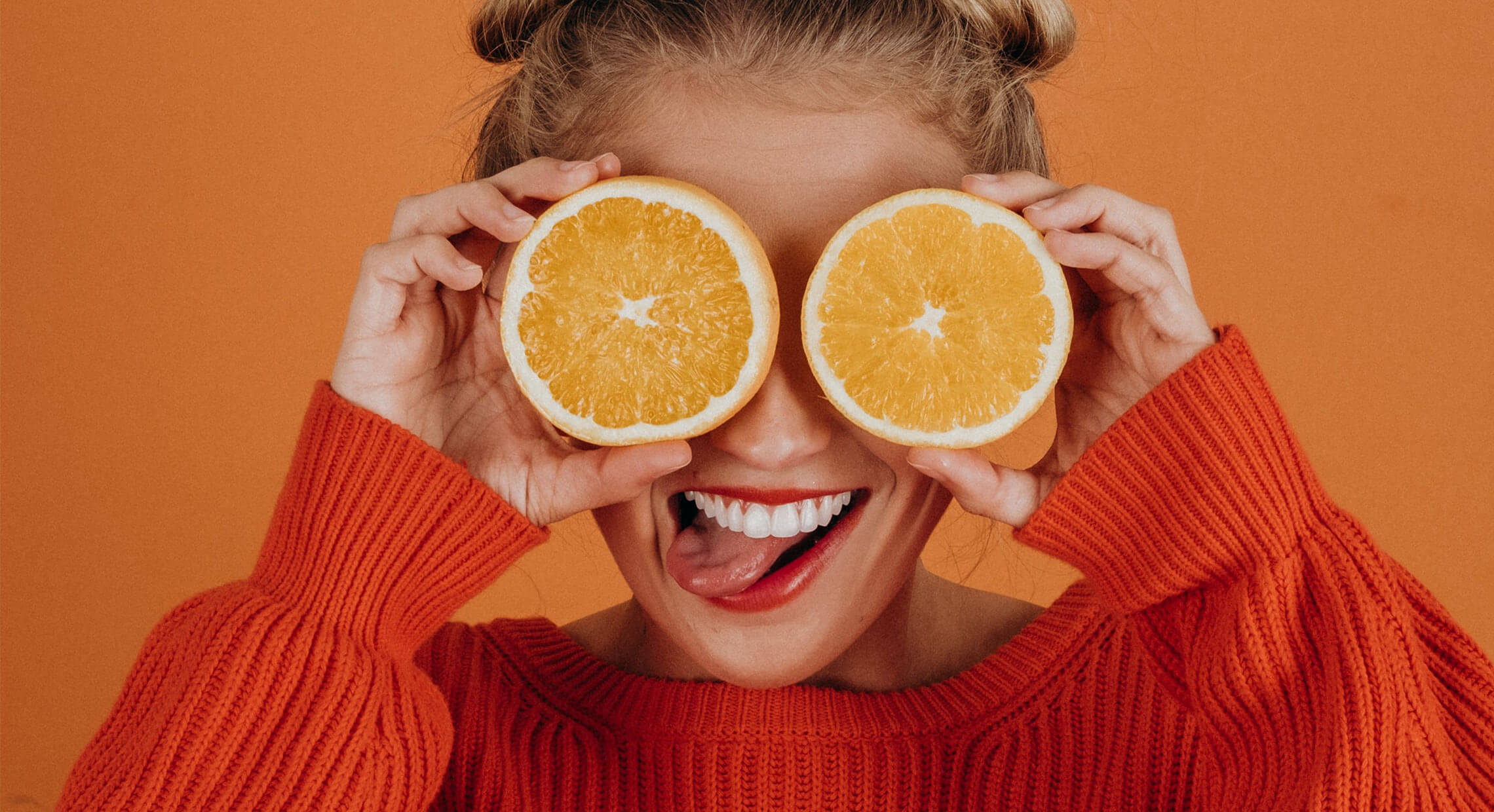 Jeune femme souriant qui tient deux moitiés d'oranges devant ses yeux