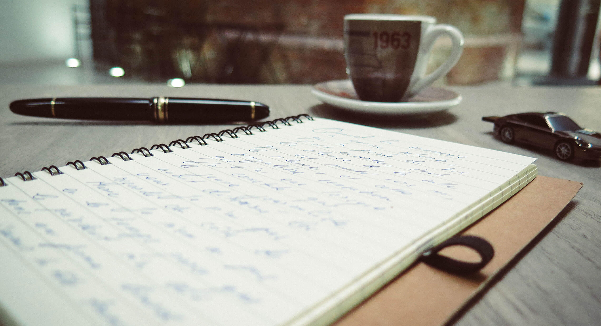 Cahier et stylo apposés sur une table de travail à côté d'une tasse a café