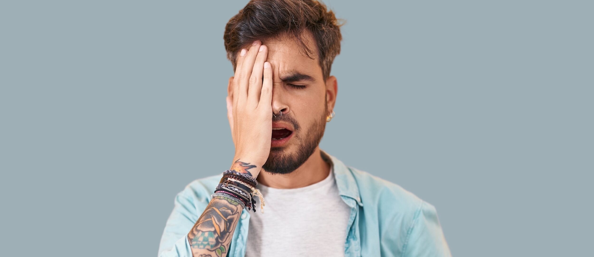 homme qui porte une chemise bleu et des tatouages, met la main sur l'oeil car il a mal à l'oeil