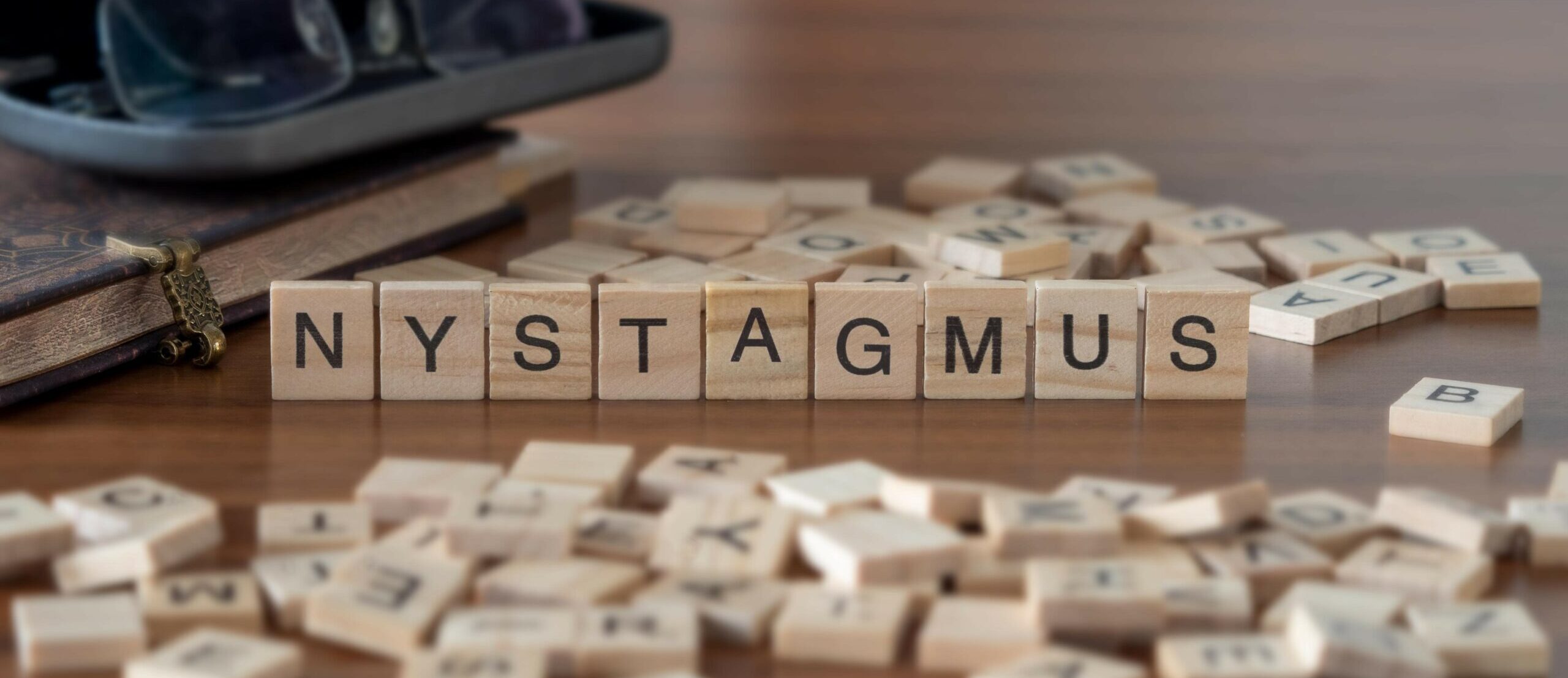 nystagmus word or concept represented by wooden letter tiles on a wooden table with glasses and a book