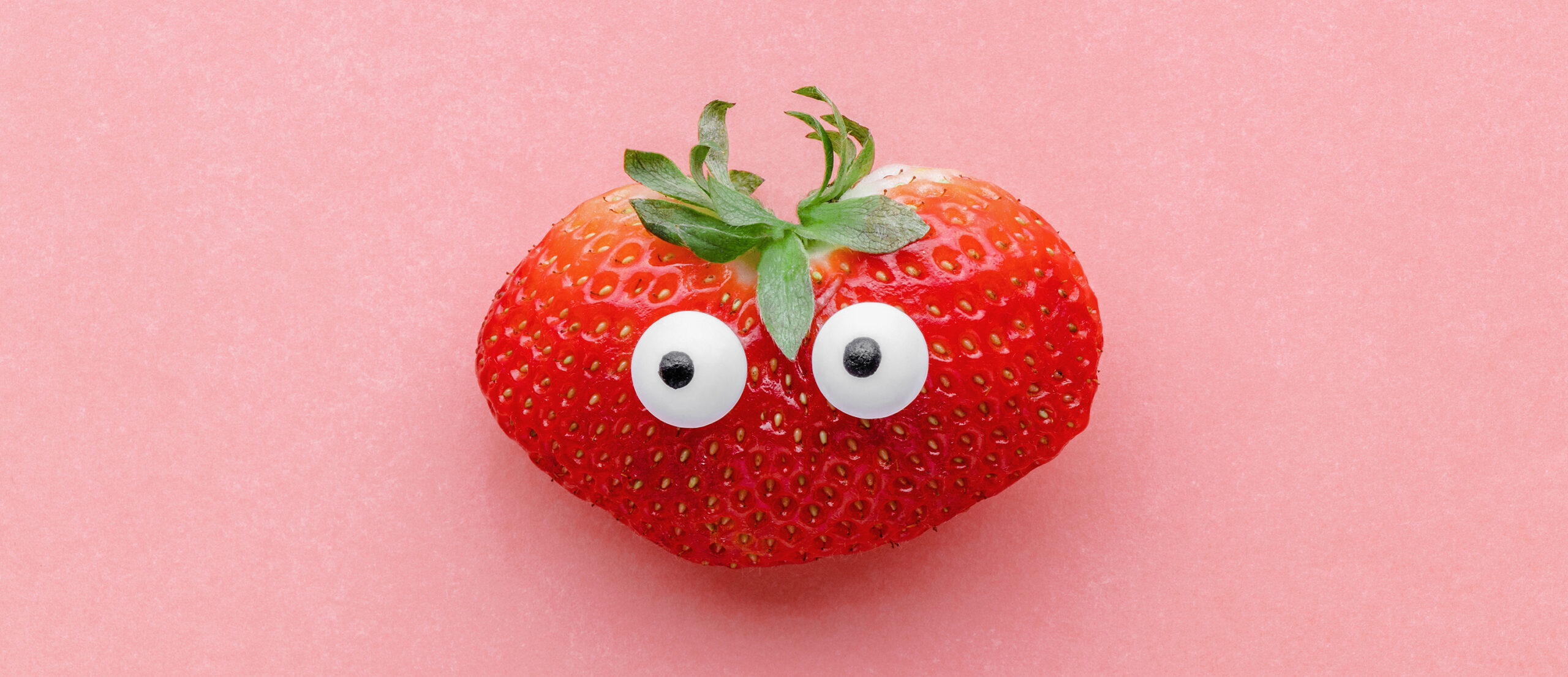 Funny face strawberry on a pink background, creative healthy food concept, top view